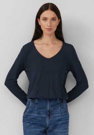 Marineblaues Langarm-V-Ausschnitt-Shirt aus Baumwollmischung, lockere Passform, mit einer glatten Textur und subtilen Nähdetails. Kombiniert mit hoch taillierten Jeans.