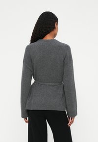 Harmaa vyöllinen neulecardigan pitkähihaisilla, pehmeällä neulepinnalla, kietaisusuunnittelulla ja ribatulla hihansuulla. Takakuvassa näkyy muotoiltu vyötärö.
