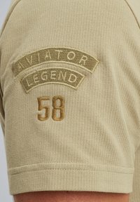 Khaki kortærmet skjorte i tekstureret stof med broderet "AVIATOR LEGEND" og nummeret "58" i brun.