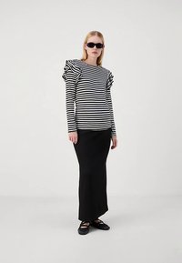 Black and white striped long-sleeve top with ruffled shoulder details paired with a black, fitted maxi skirt and flat shoes.