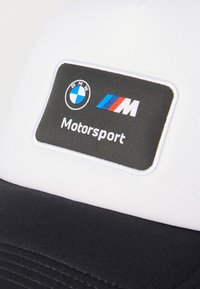 Λευκό και μαύρο καπέλο με ορθογώνιο αυτοκόλλητο λογότυπο BMW Motorsport, με μπλε, κόκκινες και λευκές αποχρώσεις ραμμένες στο μπροστινό πάνελ.
