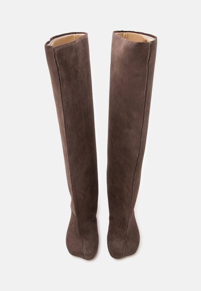 Paire de bottes hautes en daim marron avec bouts arrondis et coutures visibles à l'avant et sur les côtés, présentées debout sur fond blanc.