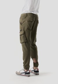 Pantalones cargo verde oliva con múltiples bolsillos laterales, puños ajustados y textura de tela. Combinados con zapatillas deportivas blancas y grises.