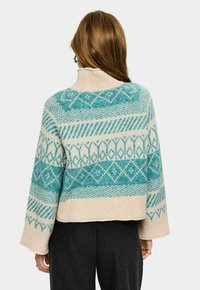 Beige och teal-mönstrad ulltröja med ribbad polokrage, med geometriska mönster och vida ärmar, kort längd.