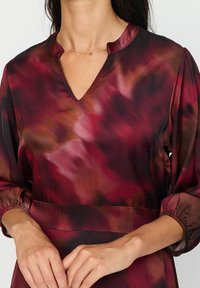 Burgunderrød og mørk rosa mønstrede kjole med v-hals, trekvart ermer og elastiske mansjetter. Glatt, lett stoff, innsnurt i midjen.