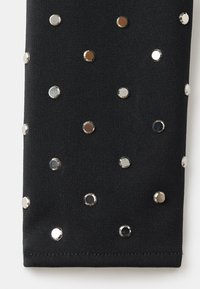 Czarna elastyczna tkanina ozdobiona rozmieszczonymi metalowymi wstawkami w kolorze srebrnym, różowego złota i czerni, tworząc teksturową i wzorzystą powierzchnię.