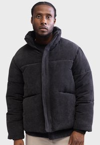 Chaqueta de plumas de pana negra con un alto cuello, diseño acolchado y bolsillos frontales. Cuenta con tejido texturizado y cierre de cremallera.