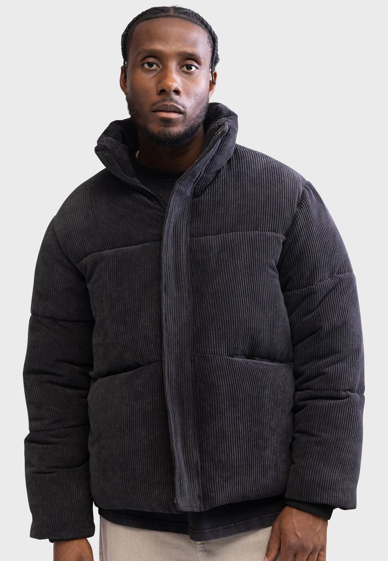 Chaqueta de plumas de pana negra con un alto cuello, diseño acolchado y bolsillos frontales. Cuenta con tejido texturizado y cierre de cremallera.