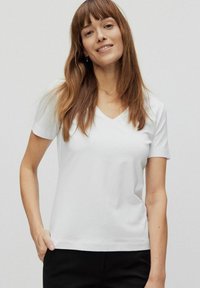 Hvid kortærmet V-hals t-shirt lavet af blødt stof, med en afslappet pasform og en glat tekstur, båret afslappet med sorte bukser.