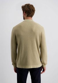 Langärmliges Strickhemd in hellem Beige mit strukturiertem Stoff, kragenförmigem Design und gesäumten Ärmeln, kombiniert mit dunklen Jeans.