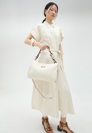 Vestido blanco texturado con cuello y mangas cortas. Elegante bolso beige con asa trenzada, herrajes dorados y detalles de diseño únicos.