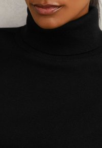 Musta poolukauluspaita pehmeästä, ribatusta neuloksesta; lähikuva, joka korostaa kaula-aukon muotoa ja sileää tekstuuria.