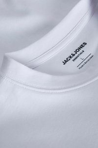 Weißes Baumwoll-T-Shirt mit rundem Ausschnitt. Mit schwarzem Drucklogo und Pflegeetikett im Kragen. Glatte Textur, schlichtes Design.