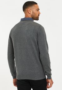 Maglione grigio con maniche lunghe, scollatura rotonda, polsini a coste e una texture liscia. La vista posteriore mostra un design aderente.