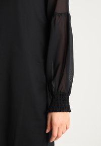 Schwarzes Kleid mit durchsichtigen langen Ärmeln, die am Bündchen gerafft sind, aus leichtem Stoff und in lässiger Silhouette.