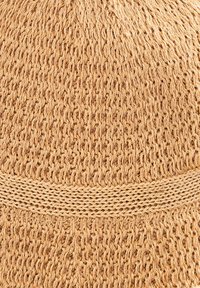 Wełniana czapka z beżowych włókien o teksturowanym wzorze. Posiada gładki, kontrastowy pas w pobliżu podstawy czapki.