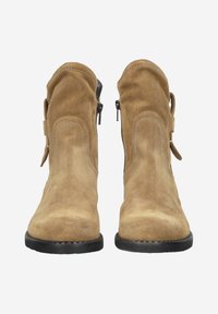 Para jasnobeżowych zamszowych botków za kostkę z czarnymi gumowymi podeszwami, zamkami błyskawicznymi po bokach i dekoracyjnym przeszyciem na białym tle.