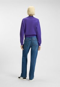 Paarse sweatshirt met een zwarte kraag, gecombineerd met blauwe recht gesneden jeans. Gladde textuur, ontspannen pasvorm en contrasterende kleurdetails.