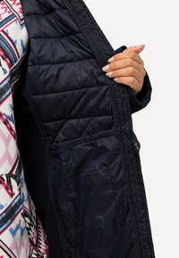 Giacca a vento blu navy con interno trapuntato, dotata di tasca laterale e una texture esterna liscia. L'interno ha una finitura morbida.