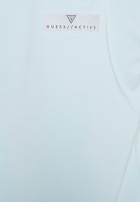 Jasnoniebieska odzież sportowa wykonana z gładkiego materiału, z metką z logo "GUESS//ACTIVE" w kontrastowym kolorze.