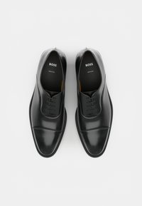 Zapatos de cuero negro con cordones, acabado liso, puntera redondeada, detalles de costura sutiles y logotipo "BOSS" en el interior. Hechos en Italia.