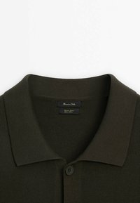 Polo en maille texturée vert foncé avec un col plié et un bouton visible en haut à l'avant.