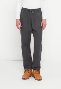 Pantaloni cargo gri cărbune cu talie elastică și șnur. Au două buzunare mari laterale. Port cu bocanci de lucru de culoare tan.