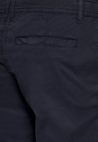 Námořnické modré bavlněné kalhoty s plochou zadní kapsou a jemnou texturou, s kontrastním švem podél pásku.