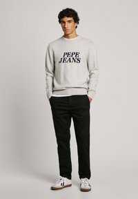 Sivi pulover s logom "PEPE JEANS", crne hlače i bijele tenisice s crnim detaljima. Pletena tekstura, rebrasti rukavi i rub.