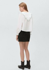 White blouse with a ruffled mint collar, long puffed sleeves, paired with a black denim mini skirt. Black ankle boots complete the look.