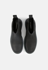 Botines de cuero negro con paneles laterales elásticos, puntera redondeada y suela de goma gris. Nombre de la marca visible en el interior.