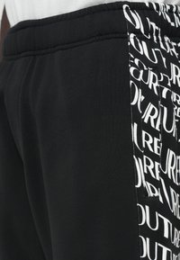 Melni svārki ar elastīgu jostasvīru, ar sānu paneli un kabatu, kas dekorēta ar atkārtotu baltu "COUTURE" teksta rakstu.