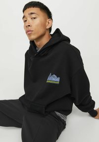 Sort hættetrøje med en stor lomme foran, der har et farverigt grafisk logo med teksten "Parks & Leisure." Blødt stof og afslappet pasform.