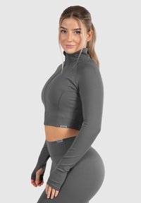 Gekürzte Sportjacke in Grau, mit hohem Kragen, langen Ärmeln mit Daumenlöchern und einer körperbetonten Passform für Sportbekleidung.