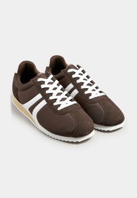 Sneaker marroni con tessuto texture e dettagli in suede, lacci bianchi e strisce bianche a contrasto. Suola in gomma per una buona aderenza.