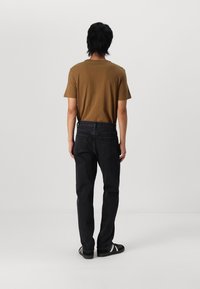 Camiseta de algodón marrón combinada con unos pantalones vaqueros negros. La camiseta tiene cuello redondo; los vaqueros tienen un ajuste holgado con dos bolsillos traseros y costuras visibles.