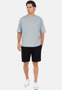 T-shirt bleu clair à manches courtes associé à un short noir. Présente une coupe décontractée, une texture lisse, et des baskets blanches avec des accents rouges.