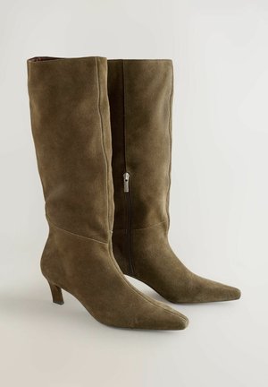Bottes en daim vert olive arrivant au genou avec un bout pointu et une fermeture éclair noire sur le côté. Présente un talon modéré et une texture lisse.