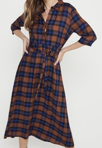 Abito midi a quadri marrone e blu con bottoni frontali, colletto, maniche a tre quarti e vita legata. Tessuto morbido con un design fluido.