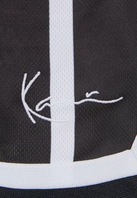 Svart atletisk tyg med vita ränder och en detaljerad vit broderad signatur. Texturerat, andningsbart nätmaterial.