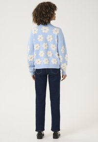 Gaiši zils adīts džemperis ar baltām ziedu rakstiem, apvienots ar tumši ziliem taisnajiem biksēm un melnām kurpēm.