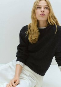 Maglione nero a maglia con collo rotondo e polsini arrotolati, abbinato a pantaloni bianchi, caratterizzati da texture lisce e una vestibilità comoda.