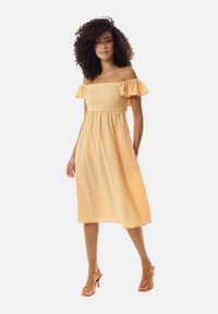 Off-the-shoulder dress in yellow gingham fabric, featuring ruffled sleeves, a fitted bodice, and a mid-length skirt. Orange strappy heels.