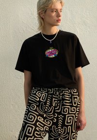 Black t-shirt with multicolor "Santa Cruz" graphic logo, paired with patterned black and white pants featuring swirl designs and a drawstring waist.