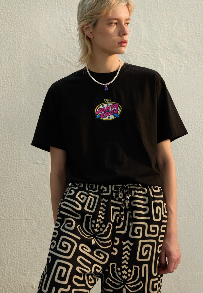 Black t-shirt with multicolor "Santa Cruz" graphic logo, paired with patterned black and white pants featuring swirl designs and a drawstring waist.