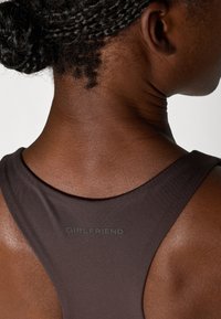 Tamsiai ruda sportinė maikutė su apvaliu kaklu, ant nugaros esantis matinio paviršiaus logotipas "GIRLFRIEND". Švelni, elastinga medžiaga.