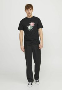 Camiseta de algodón negra con gráfico floral en rosa, blanco y verde. Combinada con pantalones anchos negros y zapatillas negras.