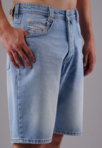Light blue denim shorts with a relaxed fit, featuring copper hardware, front pockets, and a back tag. Textured fabric with a faded finish.
