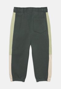 Bavlněné tepláky v tmavě zelené barvě s světle zelenými a béžovými bočními panely. Mají elastický pas a jednu zadní kapsu.