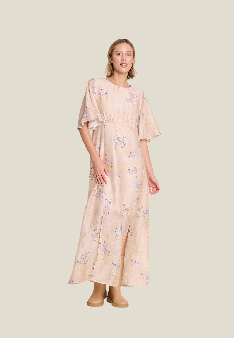 Blomsterprydet, lys rosa maxikjole med korte, flagrende ermer, innsnevret midje og sideslitt. Kombinert med beige ankelstøvler.